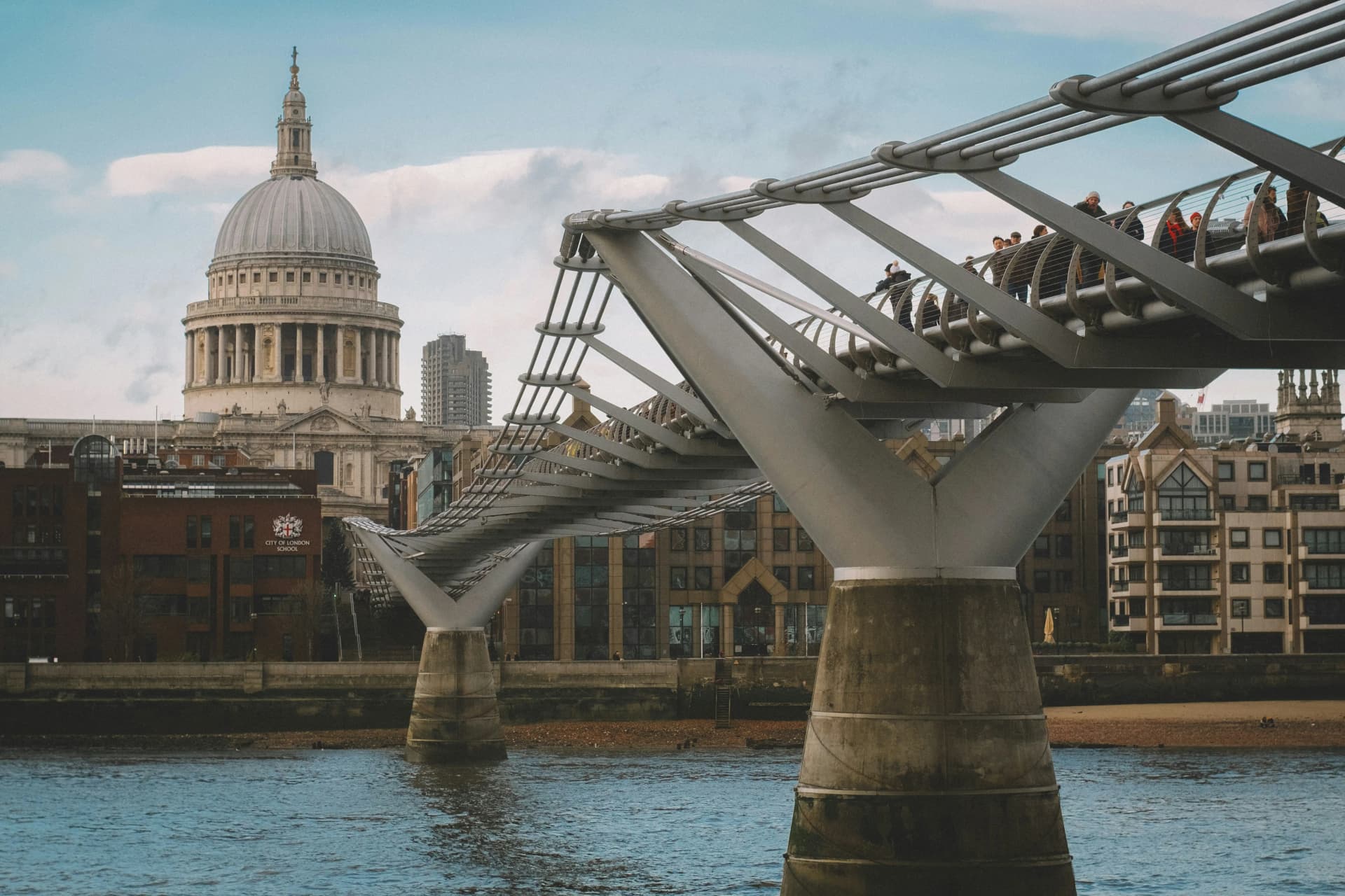 London's Millennium Bridge crossing the River Thames with pedestrians, with the dome of St Paul's Cathedral behind it